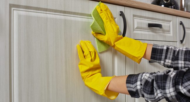 Hands in gloves with green rag is cleaning kitchen cabinets - housework and housekeeping concept. Close-up